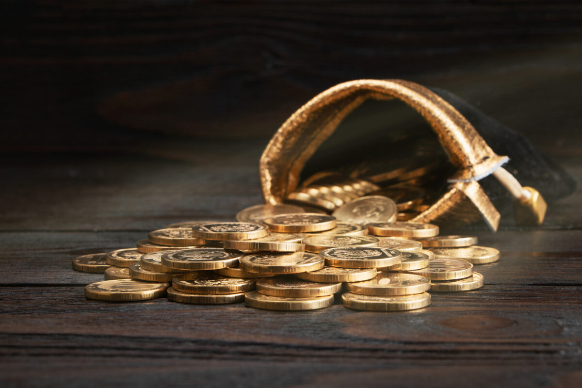 A bag with gold coins on a wooden background. The money in a black bag on a wooden table. Treasure Hunt. A Purse with money. Wallet wit gold coins