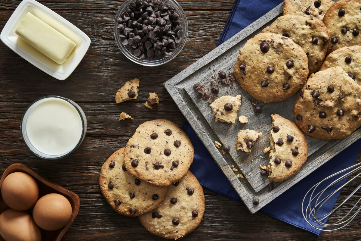 Top view of homemade chocolate chips cookies and ingredients on a rustic wooden table