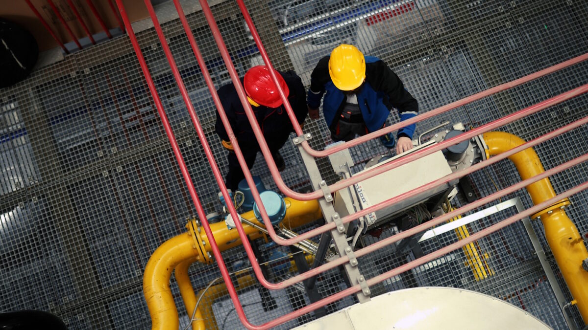 Two unrecognizable power plant workers stand in front of the control display.