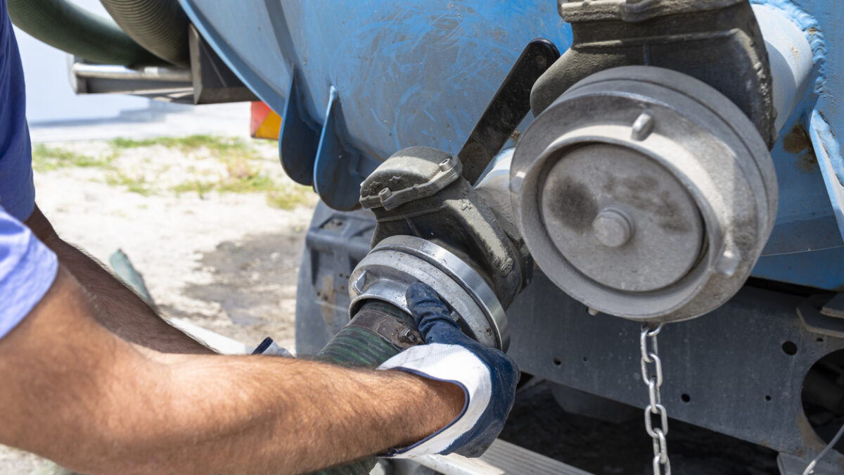 The man connects a 4 inch PVC suction hose to the flange fitting on the trucks tank.
