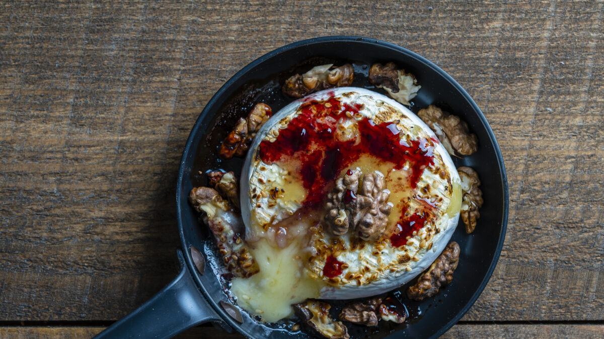 View of baked on frying pan camembert cheese, walnuts, honey and jam on wooden table background, close up, top view