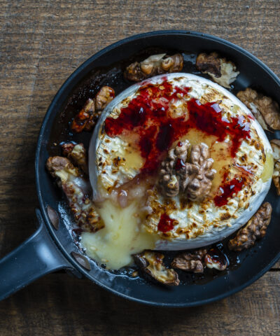 View of baked on frying pan camembert cheese, walnuts, honey and jam on wooden table background, close up, top view