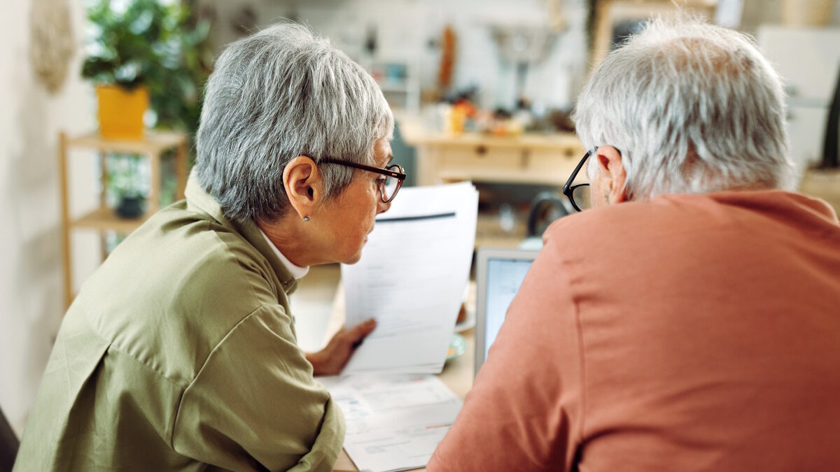 Rear view of casually clothed senior couple going over paperwork at home