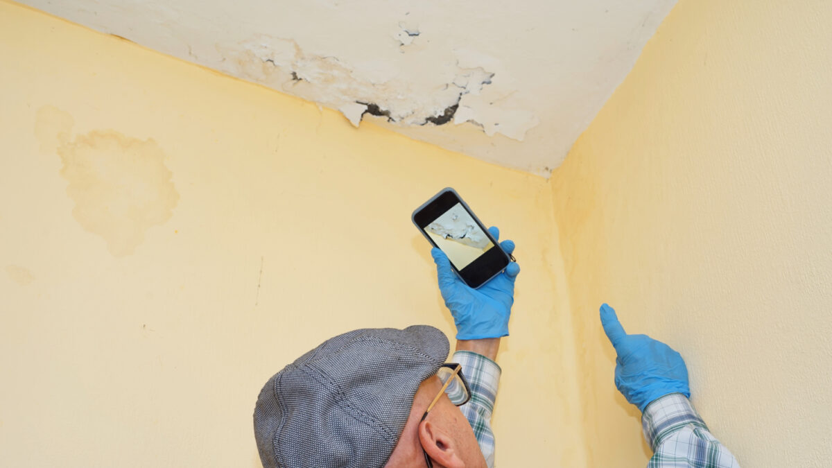 An insurance adjuster investigates an insurance claim, to determine wall and ceiling damage, using a smartphone.