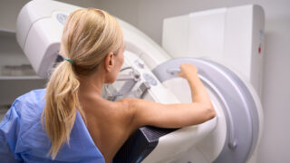 Back view of Caucasian female patient undergoing 3D mammography in radiology room