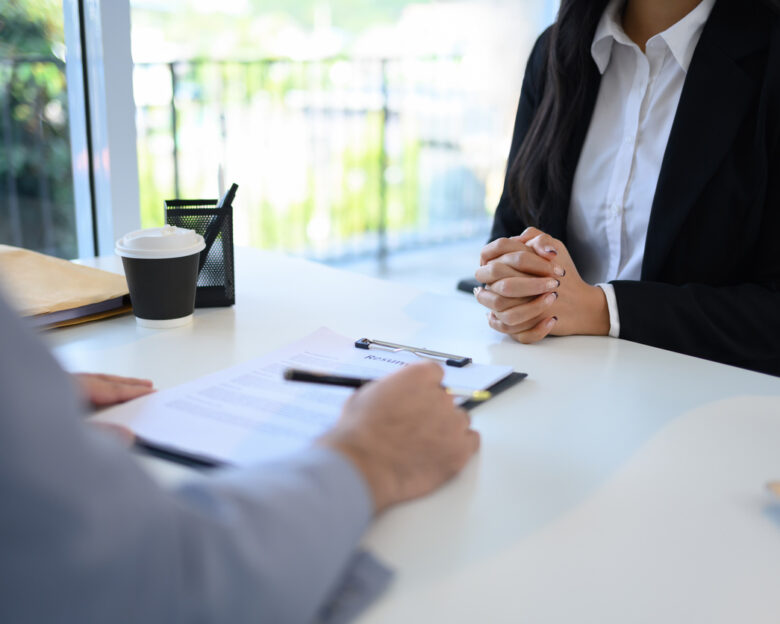 Candidate in formal wears attentively sitting across from an interviewer reviewing her resume.