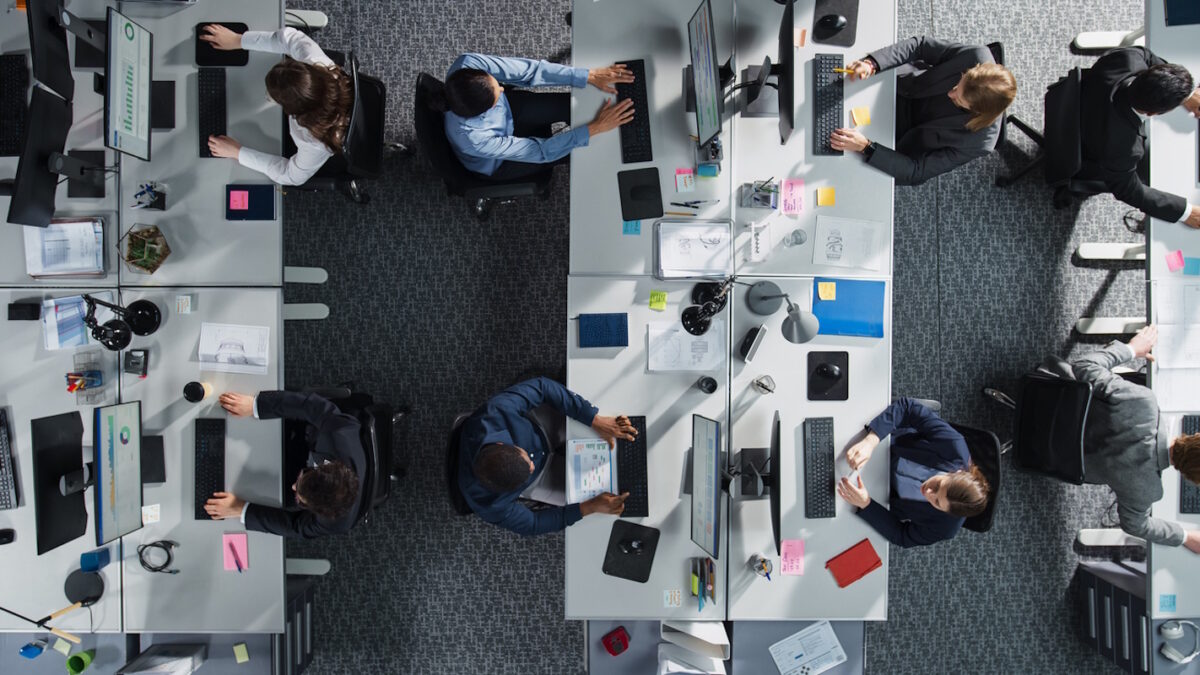 Top Down View of Diverse Colleagues Working In Corporate Office of Hedge Fund. Using Desktop Computers, Discussing Documents, Analyzing Data. Concept of Teamwork and Professional Business Environment