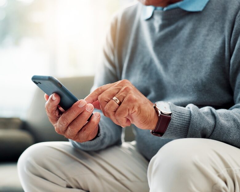 Senior man, hands and typing with phone on sofa for game, word search or social media app at home. Closeup, male person or elderly user browsing with mobile smartphone for connection or network