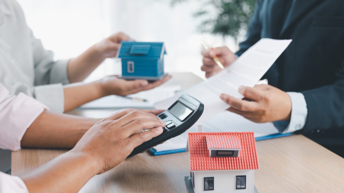 House model on desk with blurred people discussing contract in background, concept of real estate investment, mortgage loan, home ownership, property business and financial agreement.
