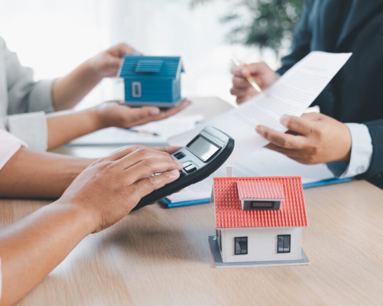 House model on desk with blurred people discussing contract in background, concept of real estate investment, mortgage loan, home ownership, property business and financial agreement.