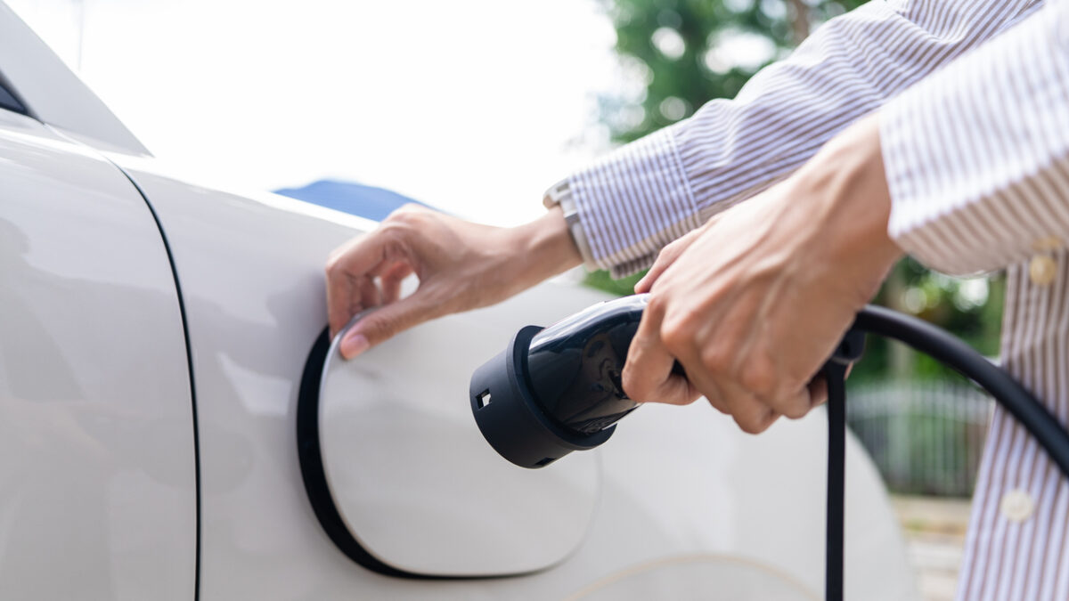 Close-up of an Asian woman's hands holding a charging plug and opening the socket of an electric car. Concept of EV charging station eco transportation and clean energy.