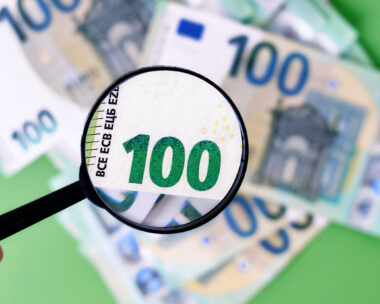 Black magnifying glass checking authenticity of 100 euro banknote