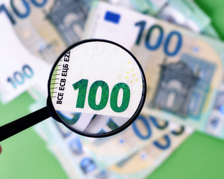 Black magnifying glass checking authenticity of 100 euro banknote