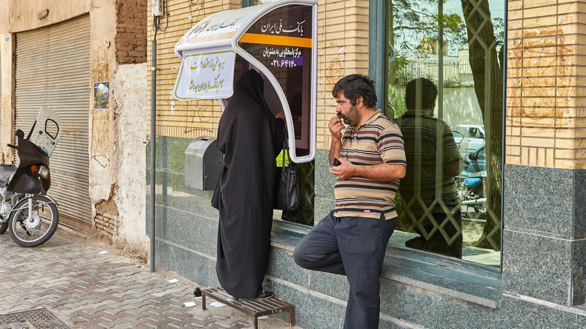 Kashan, Iran - April 27, 2017: A woman in Islamic clothes uses a street ATM, a man is waiting nearby