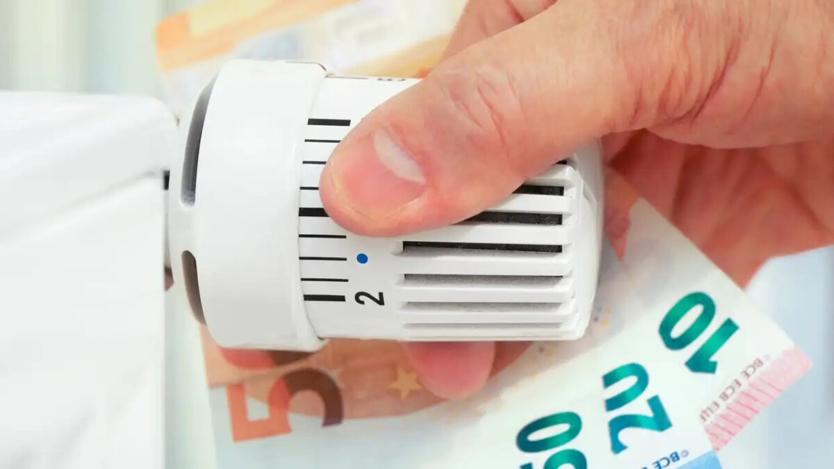 Hand on the heating thermostat with money bills, heating costs concept