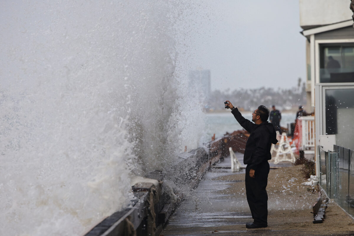 A man films from a boardwalk as waves generated by Post-Tropical Cyclone Rachel impact the coastline in Long Beach, California, US, October 11, 2026. REUTERS